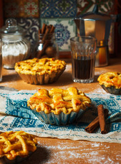 Mini homemade apple pies on rustic background with coffee,cinnamon sticks,apples,vintage towel
