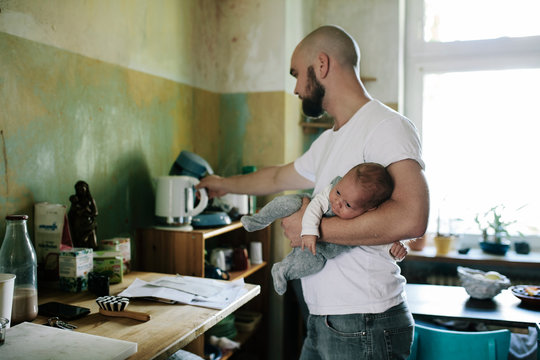 Father heating water kitchen while holding Baby