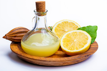 Fresh lemon juice made from ripe yellow Sicilian lemons used for cooking in glass bottle on olive wood plate