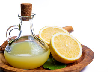 Fresh lemon juice made from ripe yellow Sicilian lemons used for cooking in glass bottle on olive wood plate
