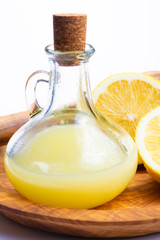 Fresh lemon juice made from ripe yellow Sicilian lemons used for cooking in glass bottle on olive wood plate