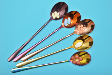 Five different types of pills in five multi colored metal spoons with long handles on blue background with copyspace