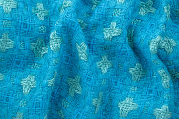 Background in the form of material from wool of blue and green color with a pattern and wavy folds, top view