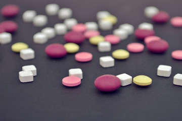 Pink, yellow round pills and white square are scattered randomly on a dark blue background, side view