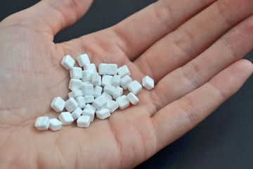 White small square pills lie in the male palm on a black background, closeup
