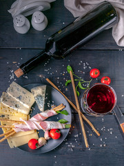 Still life glass and bottle of red wine, snacks, jamon, cheese, cherry tomatoes and arugula. Top view