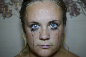 Flowed mascara on the blue eyes of the girl. Wet girl with leaking mascara in front of her eyes....