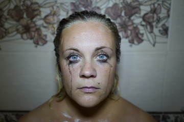 Flowed mascara on the blue eyes of the girl. Wet girl with leaking mascara in front of her eyes....