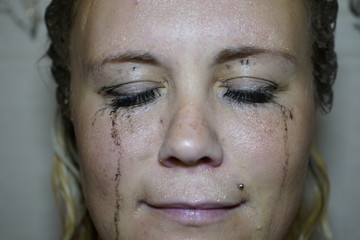 Flowed mascara on the blue eyes of the girl. Wet girl with leaking mascara in front of her eyes. Face close up.