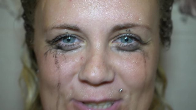 Flowed mascara on the blue eyes of the girl. Wet girl with leaking mascara in front of her eyes. Face close up.