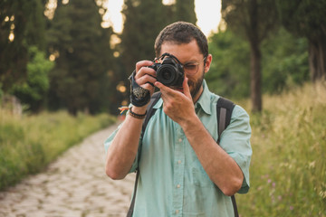 Young photographer focusing and taking a picture towards the camera in the middle of the nature