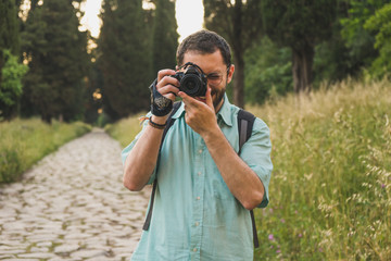 Young photographer focusing and taking a picture towards the camera in the park