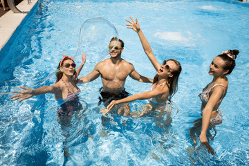 Company of young merry girls and guy are having fun with huge soap bubbles in the swimming pool on the open air on a sunny summer day