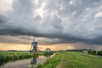 Fototapeta na wymiar Sunset with thunder clouds over a windmill along a waterside in Holland