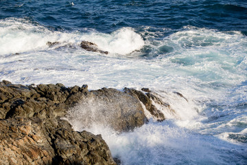 Powerful waves crashing into rocks in a mediterranean sea, blue water with foam.