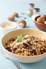 Pearl barley risotto or orzotto with mushrooms and parmesan cheese in bowl on blue concrete background. Selective focus.