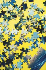 A lot of blue puzzle pieces on a yellow background. Vertical. Top view, flat lay.