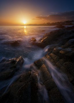 Picturesque view of clean sea water rolling and splashing near rough stones during wonderful sundown