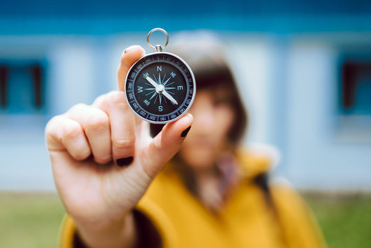 Cheerful blur young woman holding retro compass near face while standing on blurred background of countryside house