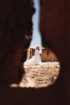 Through hole view of elegant woman in white dress inside walls of ancient fortress on daytime