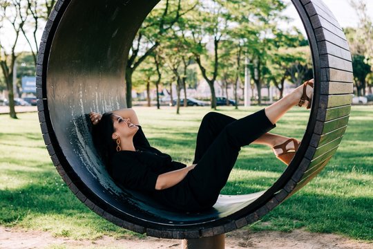 Side view of pretty woman lying in creative bench shaped as ring and smiling in Lisbon on summertime