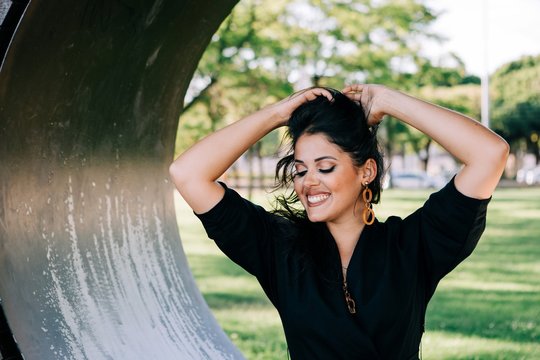 Side view of pretty woman sitting in creative bench shaped as ring and smiling in Lisbon on summertime