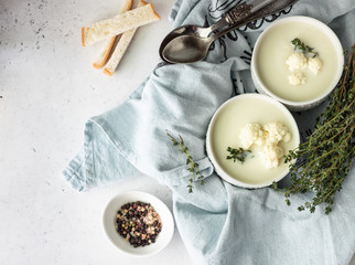 Cauliflower cream soup garnish with fresh cauliflower, thyme and bread in a white ceramic bowl....