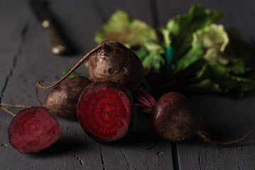 From above dark red sugar beetroots on stem with green leaves on black background