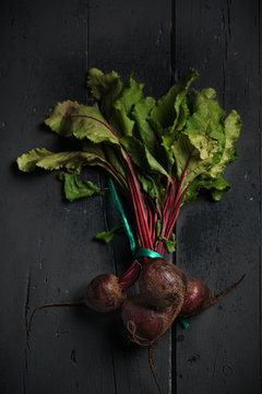 From above dark red sugar beetroots on stem with green leaves on black background