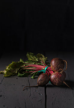 From above dark red sugar beetroots on stem with green leaves on black background