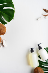 Close up of two bottles for organic body care cosmetic products on green monstera leaves, coconuts over white textile background. SPA branding mock-up, place your design of natural skincare concept.