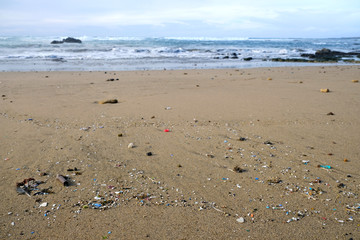 Fototapeta na wymiar Beach polluted with microplastics, ocean waves in blurred background.