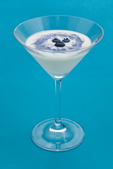 Vertical photo of fresh yogurt with blueberries in a glass on blue background as healthy dessert.