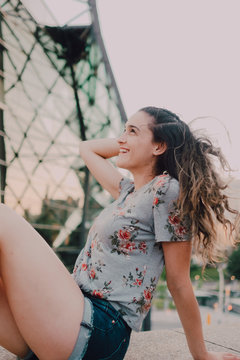 Calm content casual young woman in shorts and t-shirt enjoying sunshine while sitting on concrete parapet looking away