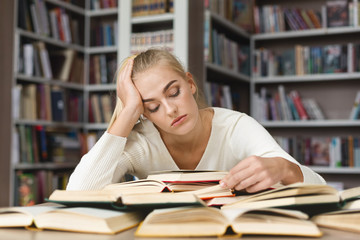 Fatigued blondy girl reading book in library