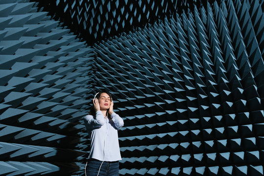 Beautiful young woman enjoying music in modern sound room with spiky walls