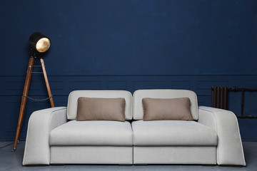 Light grey modern luxury couch with two dark pillows and vintage floor lamp at dark blue background
