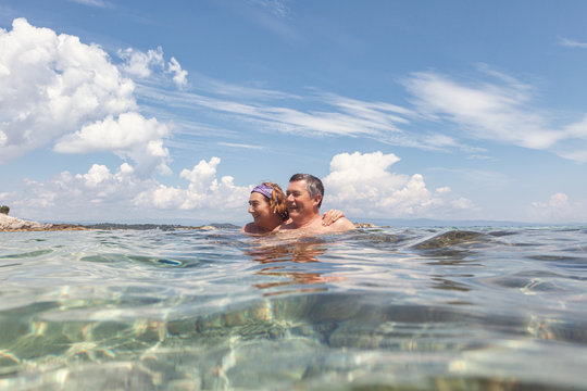 Couple of aged man and woman enjoying fresh water while swimming together in crystal water in bright day, Halkidiki, Greece