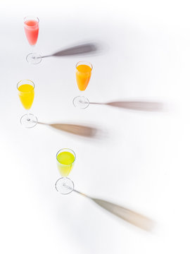 Contrasting shadows from glasses of juicy appetizing orange red yellow green drinks on white background