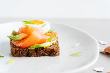 Healthy open sandwiches on multigrain wholegrain  toast with avocado, salmon, eggs, herbs, sunflower seeds over white plate on concrete background with copy space. Healthy protein food.