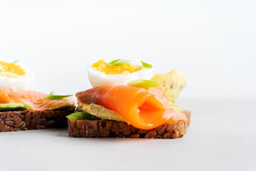Healthy open sandwiches on multigrain wholegrain  toast with avocado, salmon, eggs, herbs, sunflower seeds over white plate on concrete background with copy space. Healthy protein food.