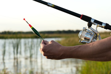 Fisherman with a rod in hands is adjusting the depth by fishing float.