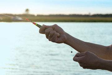 Fisherman with a rod in hands is adjusting the depth by fishing float.