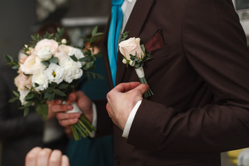 the man corrects the  boutonniere the groom with a boutonniere meeting of the groom.weedding morning.The groom in a white shirt and dark brown  suit straightens buttonhole.