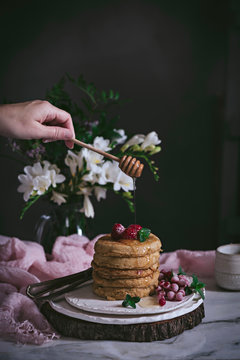 Stack of raspberry pancakes with fresh berry and dripping honey on porcelain plate at marble tabletop text to case with flowers over dark background