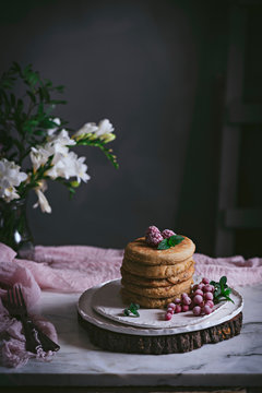 Stack of raspberry pancakes with fresh berry on porcelain plate at marble tabletop text to case with flowers over dark background