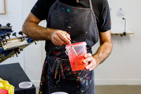Concentrated crop man wearing dirty apron mixing various paints for serigraphy in workshop