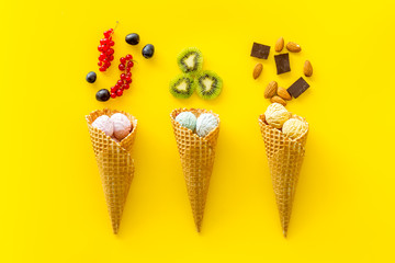 ice cream in cone with kiwi, hazelnut, chocolate and wineberry on yellow backgroung top view copyspace