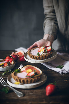 Crop person carefully serving plate of garnished citrus cake with strawberry on wooden table