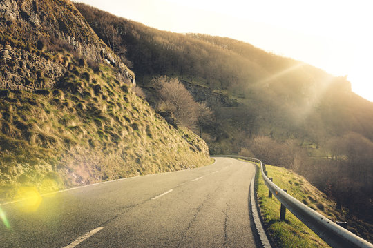 Empty winding asphalt road surrounded by low stony rocks with moss and dry bare trees